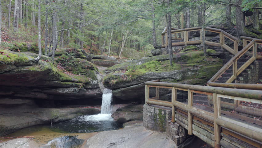 Experience Crawford Notch Park in New Hampshire, especially enchanting in the fall with charming wooden walkways and a serene waterfall, creating a breathtaking and tranquil landscape