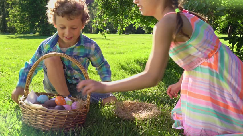 Children joyfully participate in an Easter egg hunt in a sunny park. They gather colorful eggs into a wicker basket and walk barefoot on lush grass, enjoying a cheerful spring celebration.