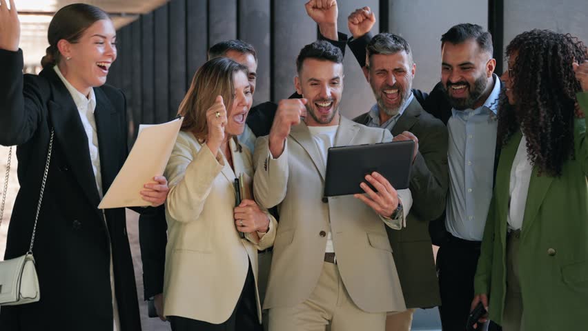 Group of young startup company businesspeople looking at tablet celebrating success achieving business goals
