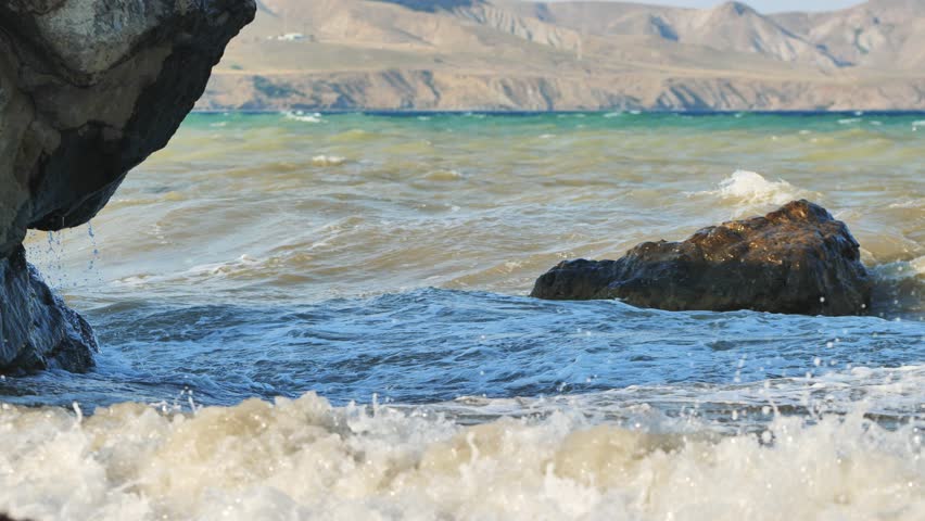 Powerful waves striking rocky crimean shoreline, mountainous terrain rising behind azure waters