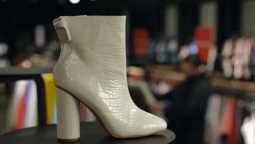 Close-up of a stylish white leather boot with a crocodile pattern in a clothing store. The boot is displayed on a black surface, showcasing its design.