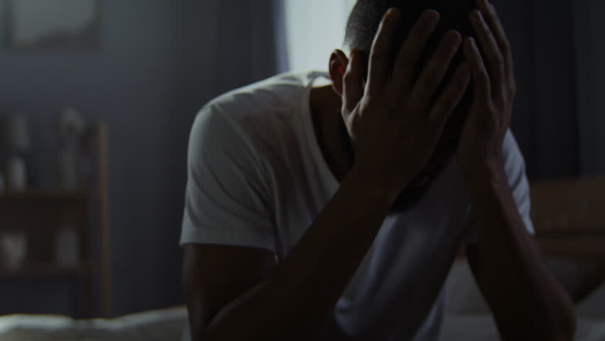 African American man hides face behind palms suffering from obsessive thoughts at home. Black guy deals with PTSR symptoms after military service