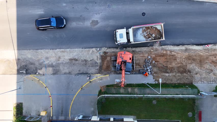 Aerial view of a construction site on a city of an excavator removing old sidewalk tiles.