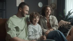 Happy mother, father and son sitting on couch in living room at home, enjoying TV show together and smiling, child holding remote control and choosing programme - Powered by Shutterstock - Get 15% off with code: PIKWIZARD15