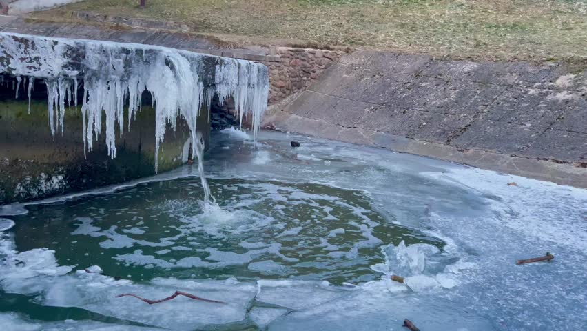 spring drip in a pond in a park icicles on a waterfall ice on water ice hole running water