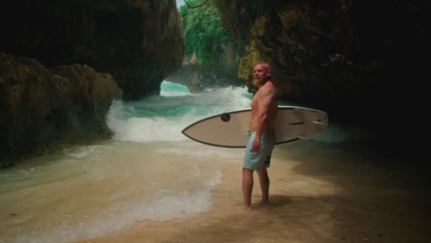 Sporty old man holds a surfboard on tropical island beach. Healthy senior man surfs in Bali, Uluwatu, make surfing. Elderly retired people enjoy outdoor active lifestyle water sport. Adult man surfs. - Powered by Shutterstock - Get 15% off with code: PIKWIZARD15