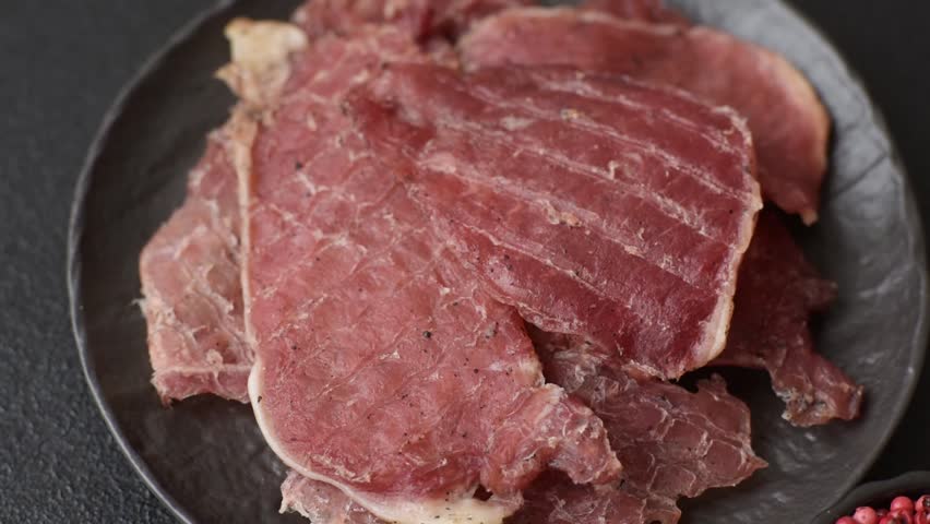 Jerky, dried pork meat slices with salt and spices on a dark concrete background
