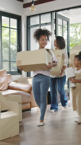Vertical Screen : Happy African American young family bought new house. Mom, Dad, and child happy hold cardboard boxes for move object and having fun laugh into modern home. New real estate dwelling.