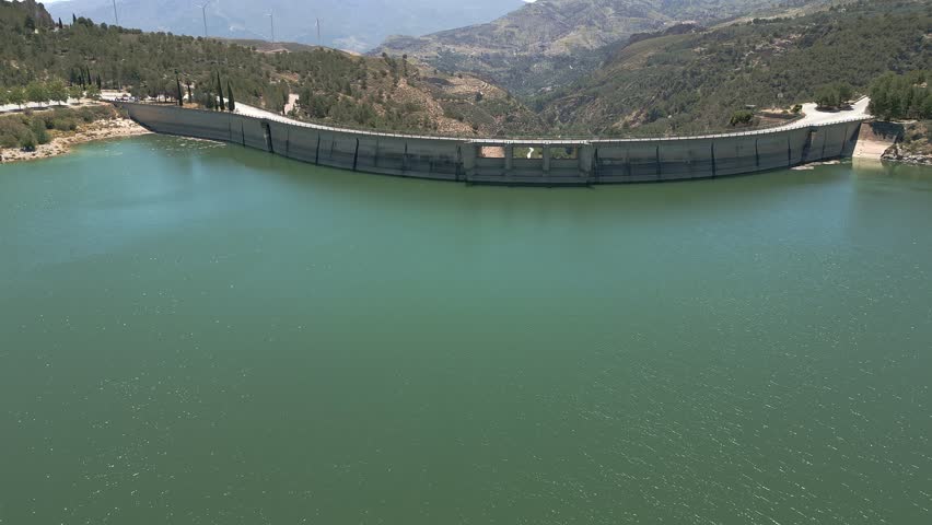 Vault dam. Panoramic aerial view in ascend of road over curved dam. Spain.