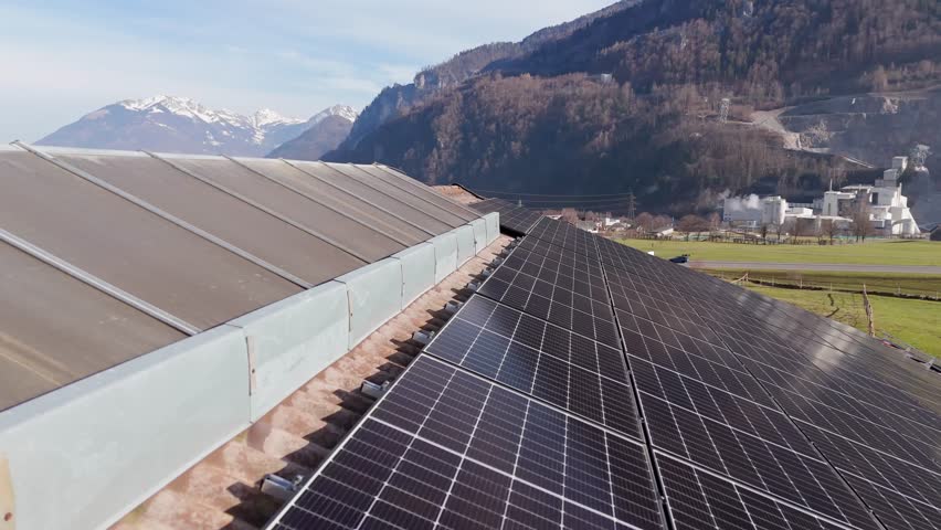 Aerial Close up of modern solar panel house and driving cars on mountain road. Alps and housing area of Switzerland in distance. Wide shot.