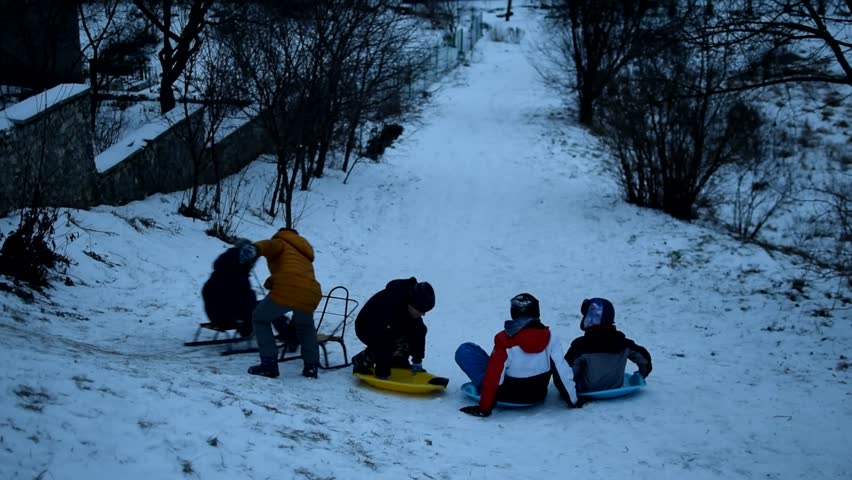 Group of children in winter clothes riding one sled going down snow slope