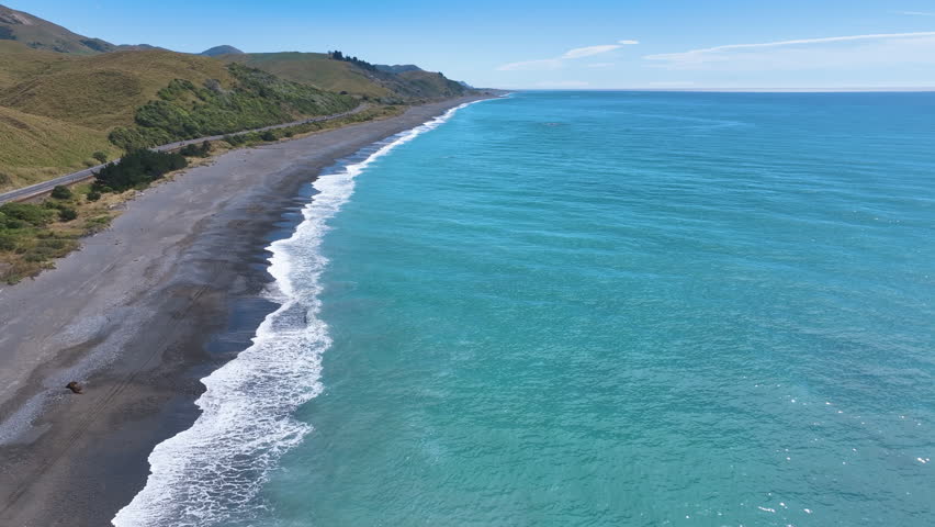 Flight north over the aqua blue ocean and waves breaking gently on Black Sand Beach Kekerengu Kaikoura Coast New Zealand