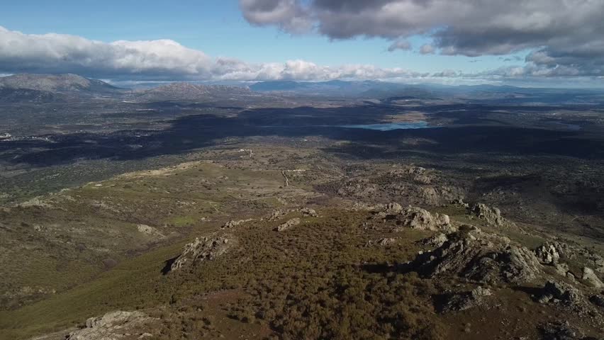 A panoramic view from a mountaintop reveals a breathtaking landscape. Rolling hills, valleys, and distant mountains stretch out towards the horizon.