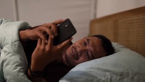 Asian man Using Smartphone in Bed at Night. Smiling guy Browsing Social Media, Romantic Chat, Dating Apps, Doing Internet Online Shopping on Mobile Phone - Powered by Shutterstock - Get 15% off with code: PIKWIZARD15