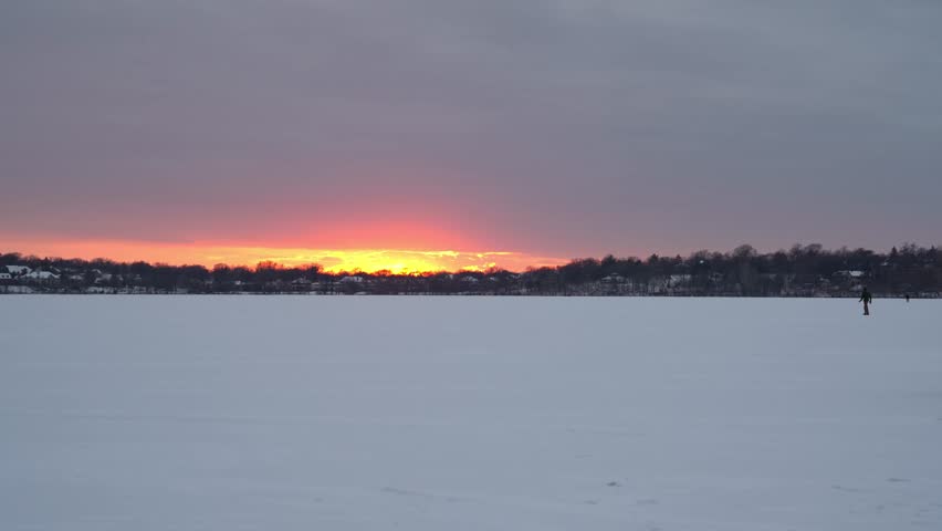 Stunning winter sunset casts warm orange and yellow hues over a vast frozen lake in Minnesota, creating a peaceful and serene landscape
