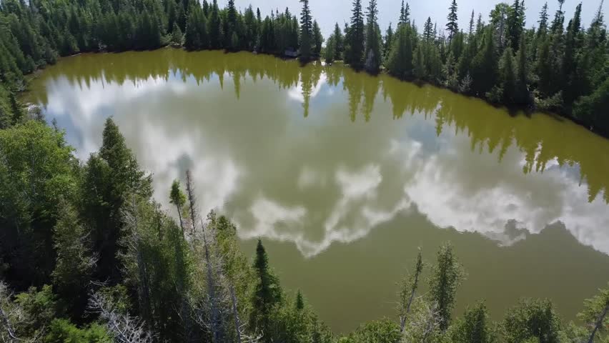 Aerial view of a small brown lake separated from a blue lake by a strip of green forests, reflecting the blue sky and white clouds. Matapedia Lake, Quebec, Canada.