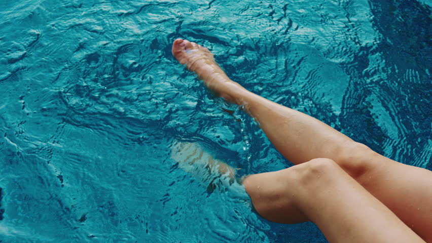 Woman swings legs in water enjoying peaceful moment by swimming pool closeup. Lady playfully dangle feet in refreshing water embodying essence of serene holiday. Travel hobby