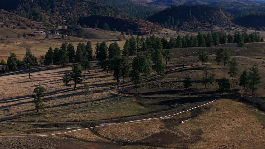 Expansive aerial view of Colorado ranch land with rolling hills, trees, and mountains