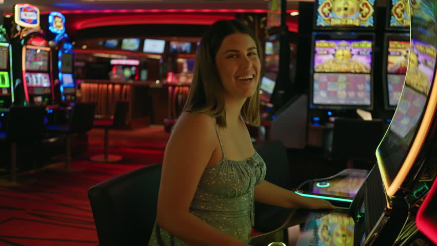 A smiling woman enjoys playing slot machines in a vibrant casino atmosphere, radiating excitement and leisure.