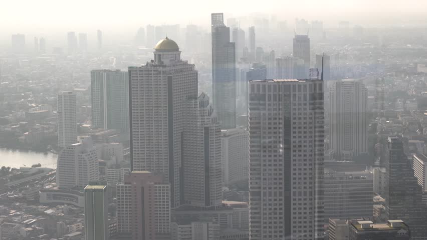 hand-held shot of large skyscrapers under smog in downtown bangkok