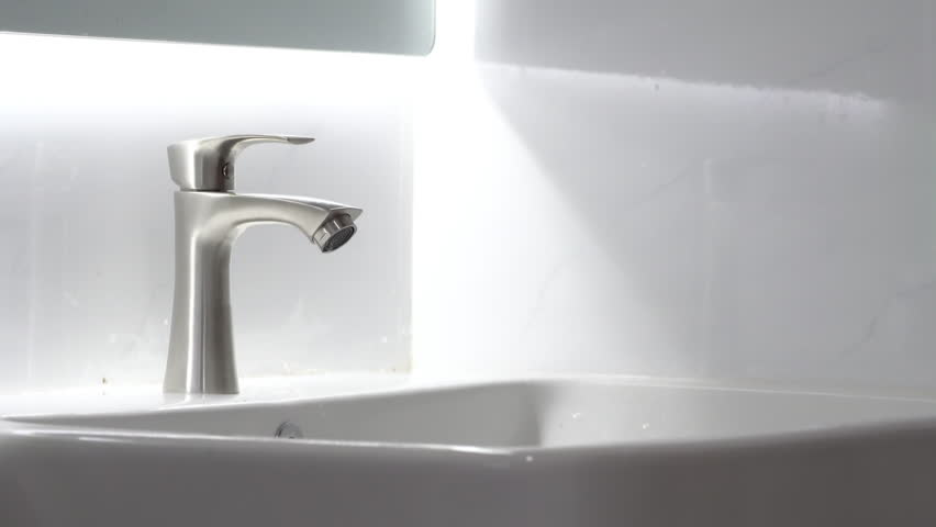 Hand turning water tap for pouring water into sink in bathroom.
