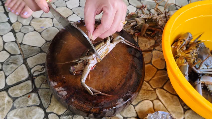 Hands chopping with a butcher knife and peeling fresh crabs on a wooden board emphasize culinary preparation and seafood cooking.