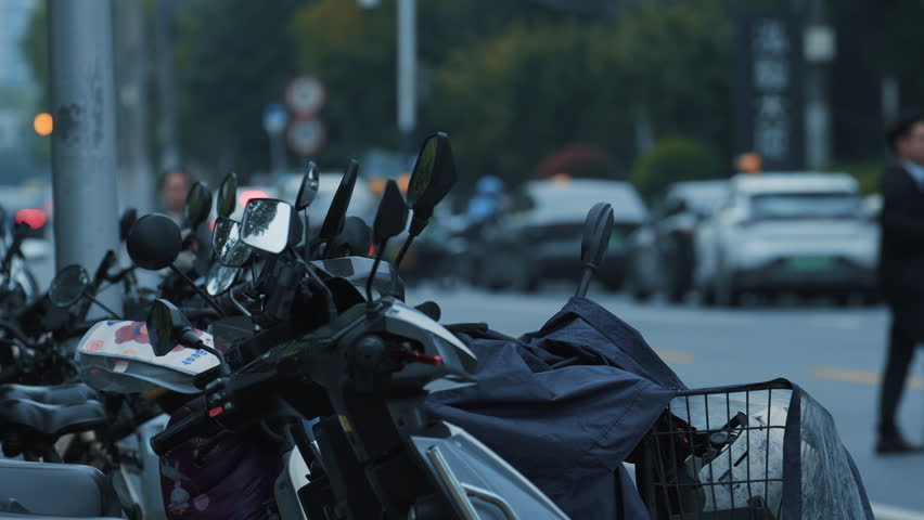 Parked mopeds in a row on the street during the day, close view of the scooters handlebars and mirrors.