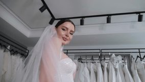 A happy slender woman poses in a wedding dress with a long veil in a wedding salon against the background of many different dresses, she holds a long veil and rotates, the camera rotates 360 degrees. - Powered by Shutterstock - Get 15% off with code: PIKWIZARD15
