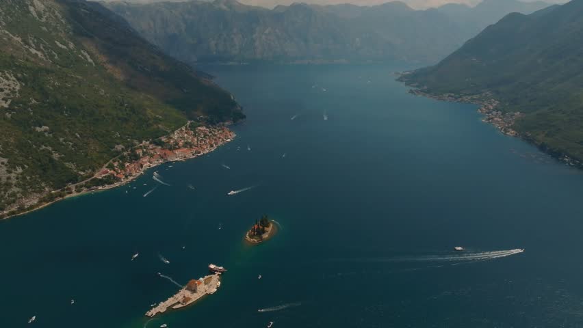 Aerial drone view of two islands Our Lady of the Rocks and Island of Saint George with churches and numerous tourist boats in Kotor Bay, with mountains in the background, Montenegro, Europe