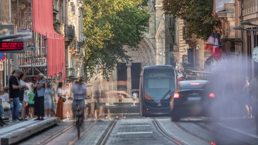 Timelapse of Bordeaux Cathedral entrance (Cathedrale Saint Andre) from Vital Carles street, featuring a moving tram in the historic city. People wait at the tram stop. A symbol of heritage. France