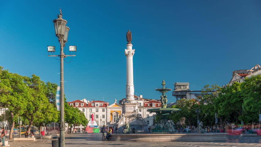 Timelapse hyperlapse of Rossio Square with wavy cobblestones, fountain and Pedro IV monument at sunset. Traffic and Santa Justa Elevator in the background. Lisbon, Portugal