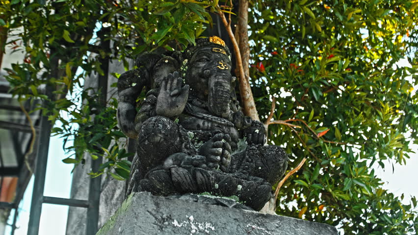 An old stone statue of Ganesha covered with moss, standing on the street