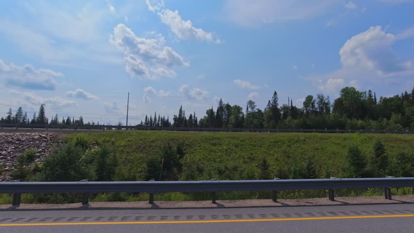 Beautiful summer view of a highway weaving through Canadian forests. Scenic driver POV side plate while travel by camper van. Driving plate road trip along the asphalt road from motorized RV, Canada.