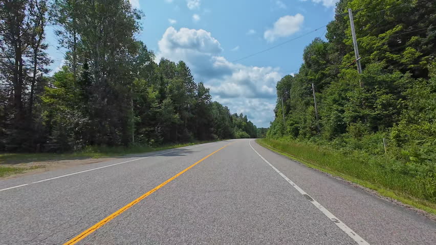 Beautiful summer view of a highway weaving through Canadian forests. Scenic driver POV front plate while travel by camper van. Driving plate road trip along the asphalt road from motorized RV, Canada.