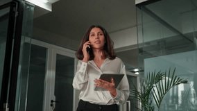 CEO entrepreneur businesswoman walking in office, talking on mobile cellphone with clients, partners. Female business executive manager having communication call, working remotely on startup project - Powered by Shutterstock - Get 15% off with code: PIKWIZARD15
