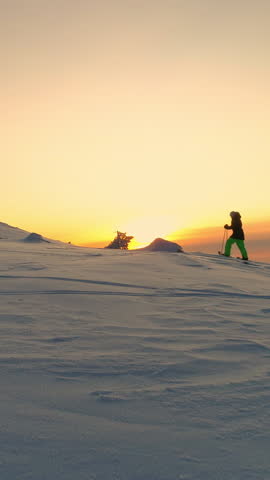 AERIAL Active woman in winter clothes snowshoeing on snowy mountain slope at sunrise. Young woman snowshoe hiking at winter sunset. Traveler snowshoe exploring snowy Lapland mountains in sunny morning