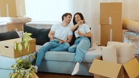 Young couple move into new apartment. Guy hold tablet in hand and point forward. Sit together with his girlfriend on sofa. Planning to put furniture in room. - Powered by Shutterstock - Get 15% off with code: PIKWIZARD15