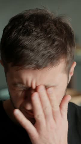 Tired man rubbing his eyes and pinching bridge of his nose. Close up of male face showing signs of stress, fatigue, or headache..Concept of exhaustion, overwork, mental health or everyday struggles