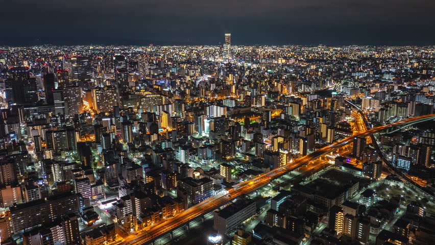 Amazing aerial panoramic shot of metropolis in evening. Busy roads and illuminated high rise buildings in urban boroughs. Night hyper lapse. Osaka, Japan
