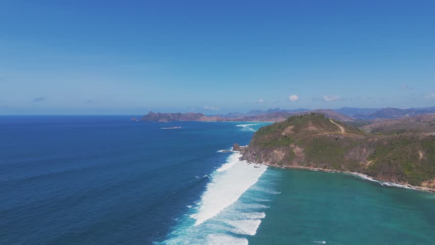 Aerial view of Lombok coastline with rugged cliffs meeting the deep blue ocean. Waves crash against the shore, creating a stunning natural seascape with breathtaking island views.