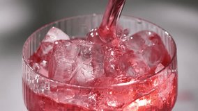 fresh red drink pouring into a cocktail glass with ice cubes on a gray sunny restaurant tabletop, slow motion, zoom in - Powered by Shutterstock - Get 15% off with code: PIKWIZARD15