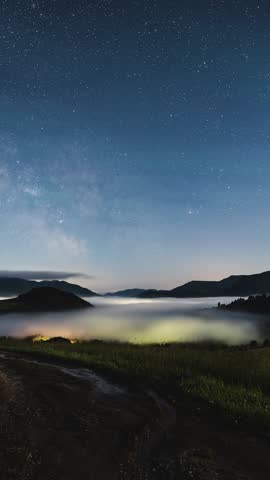 Vertical view of milky way galaxy stars in starry night sky over misty countryside Time lapse