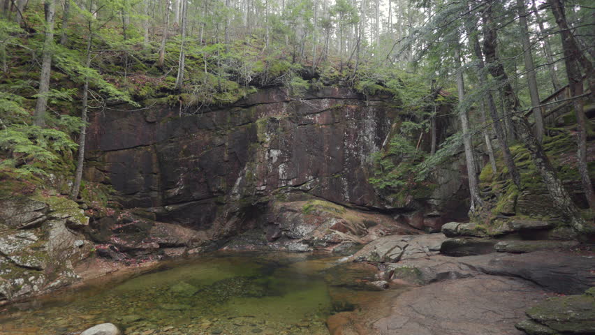 Explore the serene beauty of Crawford Notch Park in New Hampshire, where stunning rock formations and tranquil waters are nestled in a lush forest during the beautiful fall season