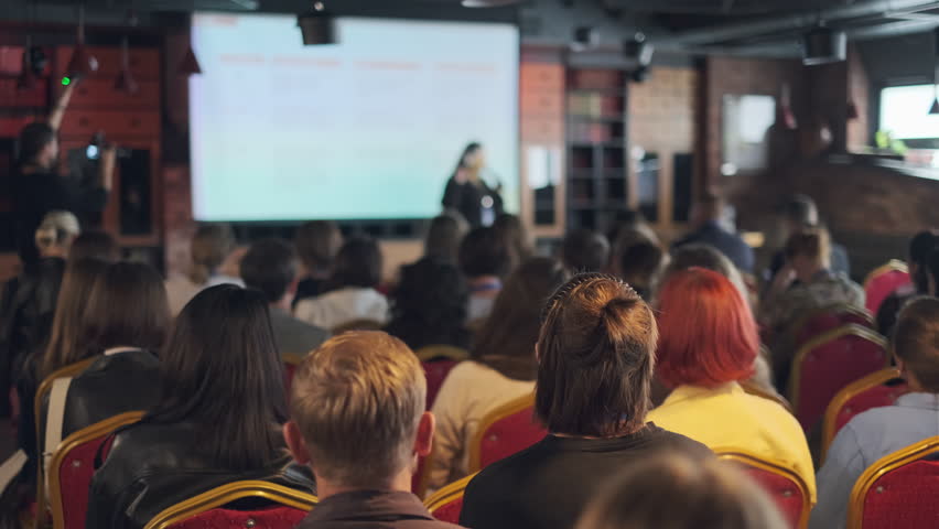 Group of people seated and focused on a presentation given by a speaker on stage