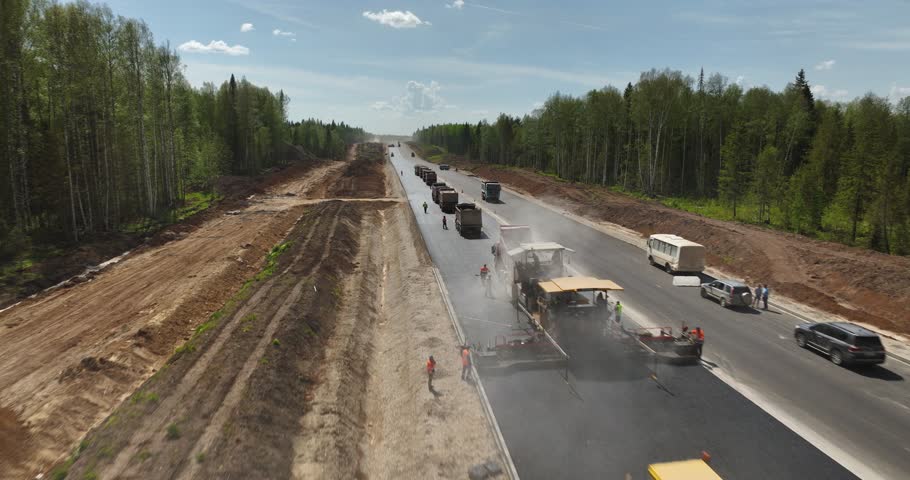 Asphalt paver unloads hot asphalt, bitumen onto the road, lays the asphalt. Road construction. Construction of a new road. Roller rolling fresh hot asphalt on the new road.