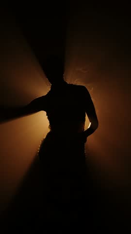 Silhouette of a woman dancing gracefully in smoke illuminated by soft, radiant light