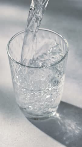 fresh clean water pouring into a glass on a gray sunny kitchen tabletop, slow motion
