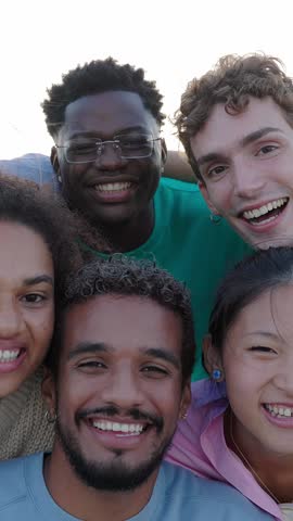 Vertical HD video portrait group of happy young gen z friends smiling at camera outdoor. Millennial diverse people relaxing together over urban background. Friendship and youth lifestyle concept.