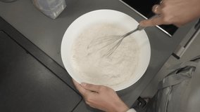A woman mixes flour, milk, and eggs in a bowl with a whisk. She prepares food in her home kitchen, mixing ingredients for the batter. Step-by-step tutorial for making pancakes with a homemade recipe. - Powered by Shutterstock - Get 15% off with code: PIKWIZARD15