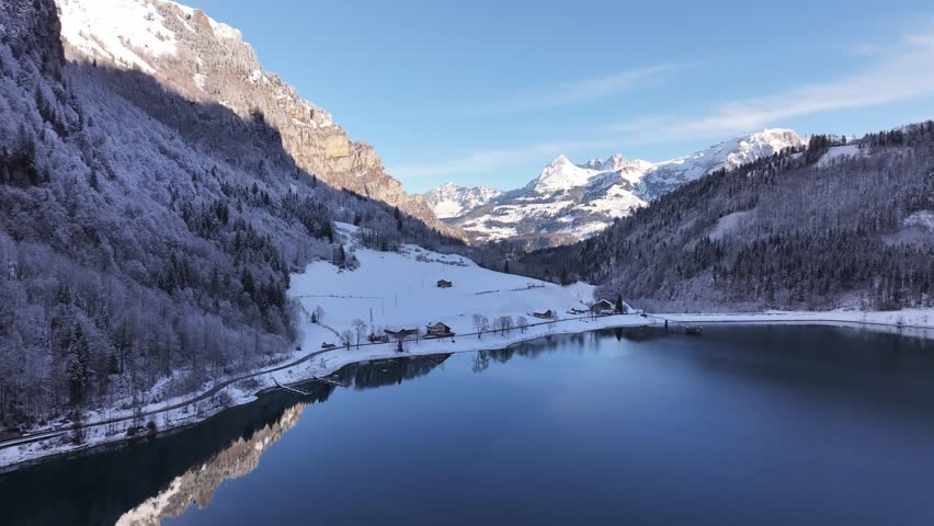 Winter wonderland. View of Lake Klöntalersee in Klöntal, Switzerland. Snow-capped mountains tower over the frozen lake, creating a magical winter wonderland.